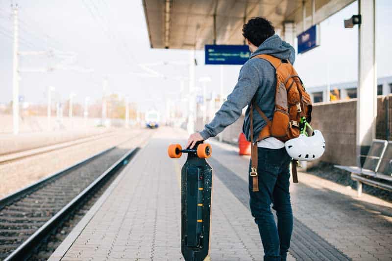 man waiting for train with electric skateboard in his hands